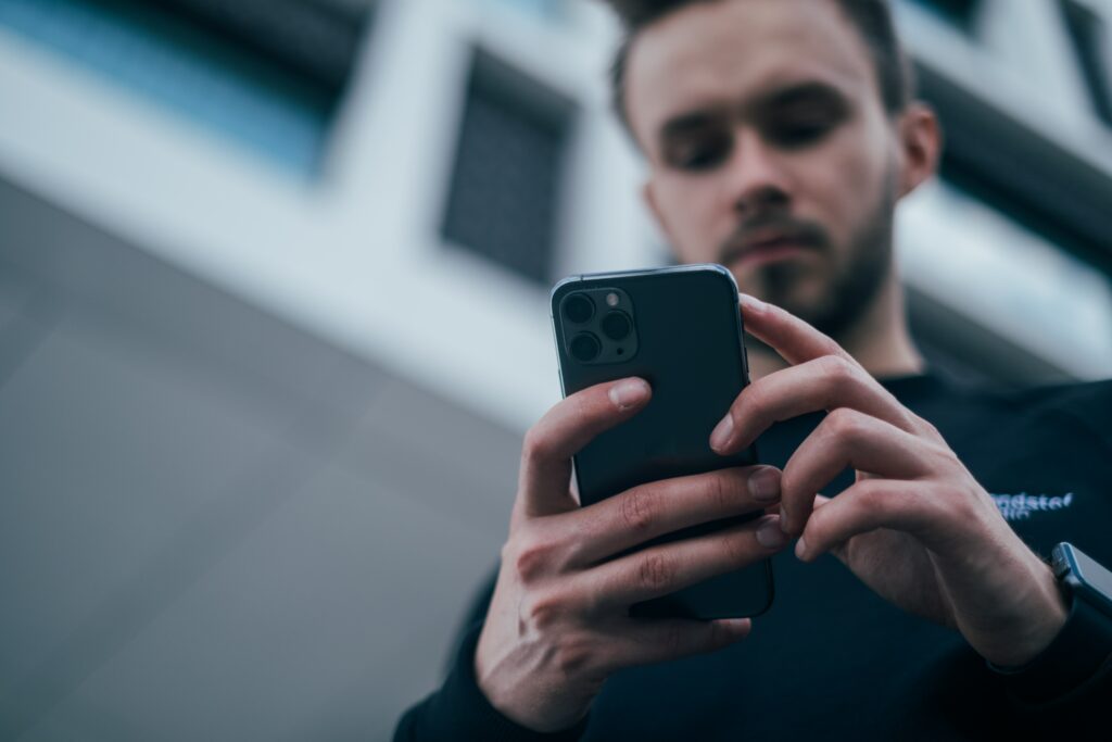 A close up a man holding his iPhone. The man in slightly blurred and the phone is clear, making the phone and his hands the focus of the shot